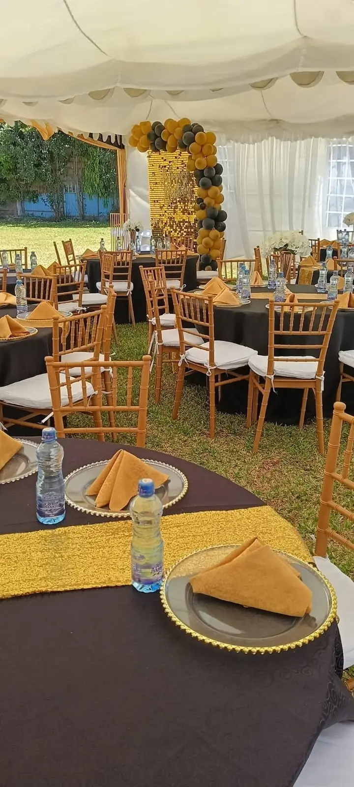 A tent dressed in gold and black with round tables, balloons and set places at Vipe Fun Park