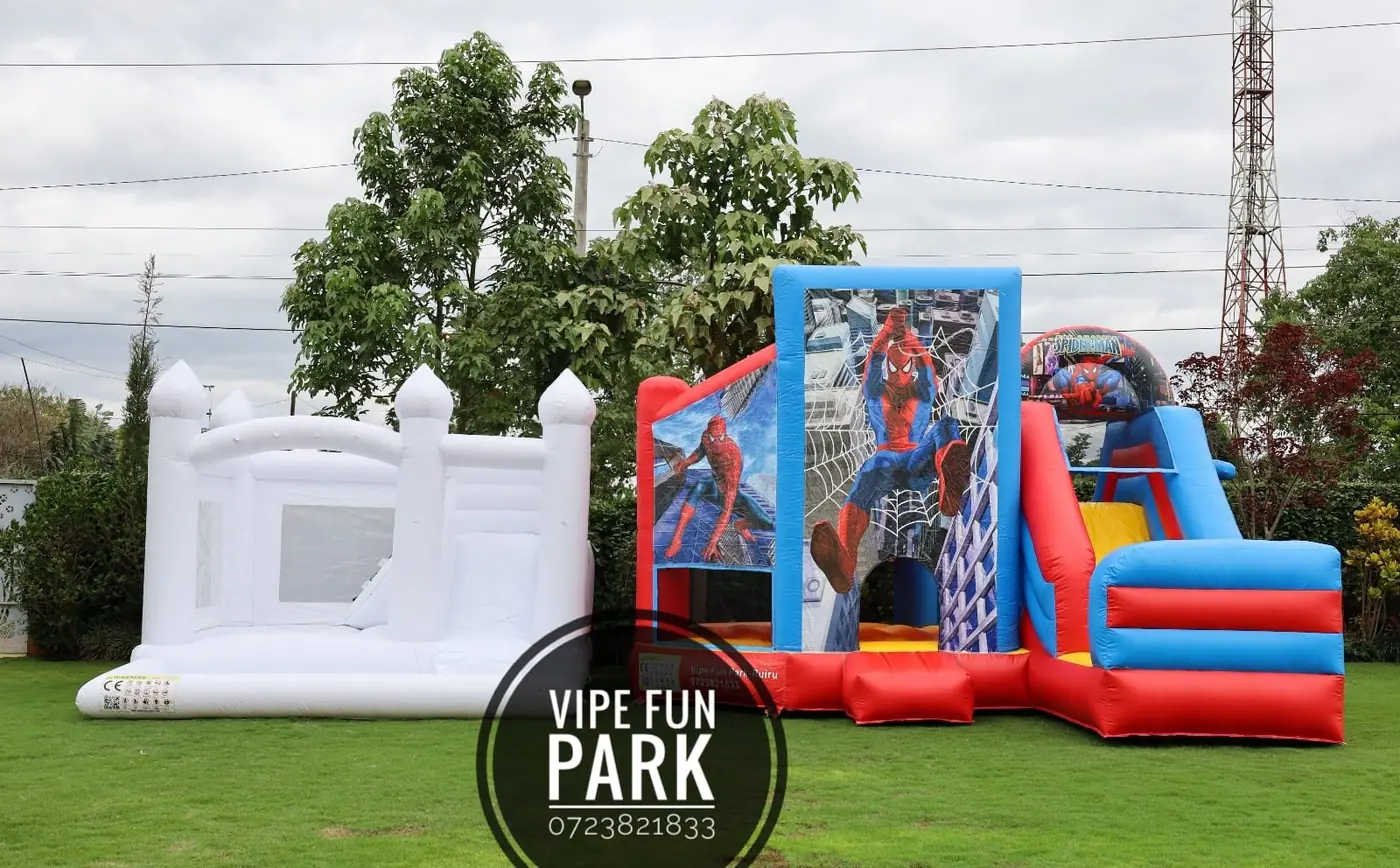A white bouncing castle beside a red and blue superhero-themed inflatable on the lawn