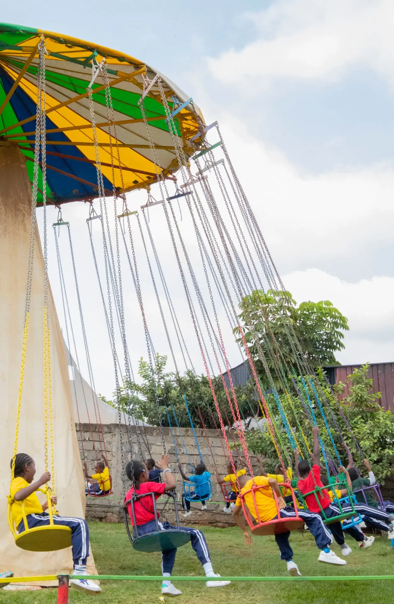 A wide view of school children photographed from behind on the colourful swing ride