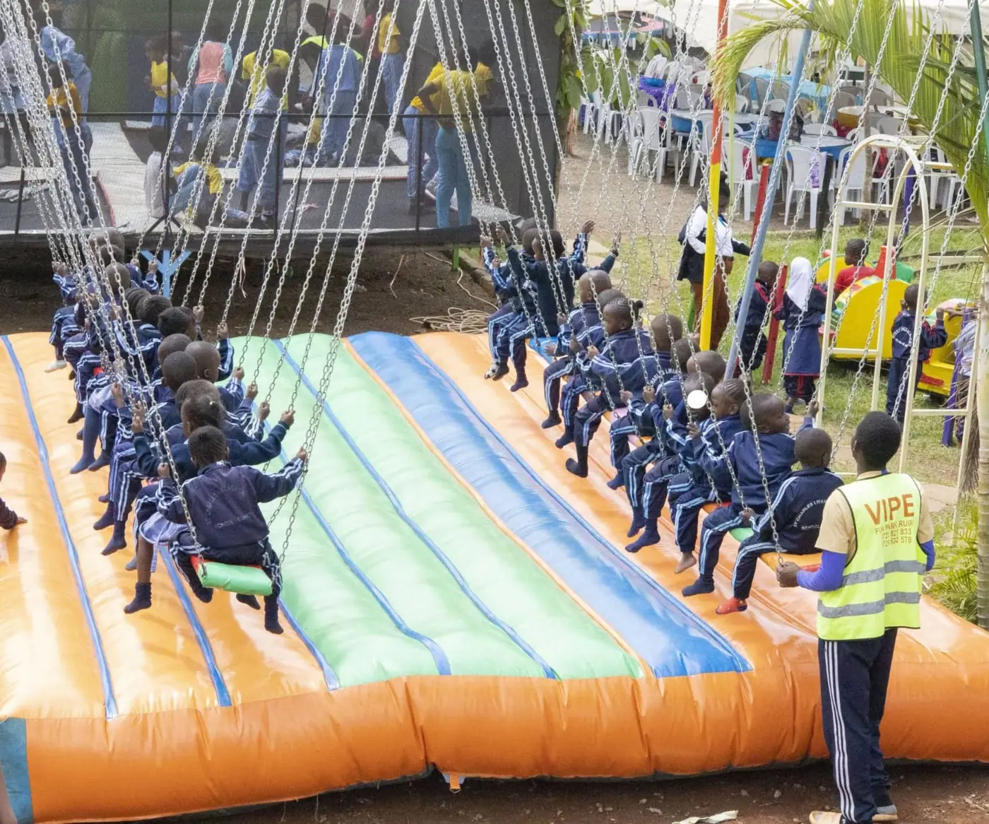 A school group photographed from behind riding the chain swing beside the trampoline